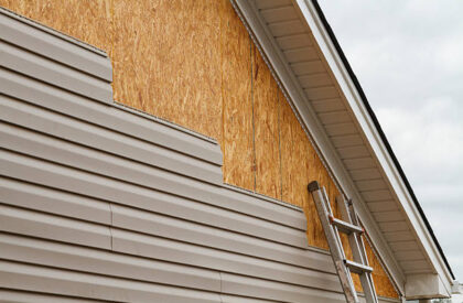 New beige vinyl siding being installed over an osb (oriented strand board) substrate on a residential house in the Southeastern USA region on a cloudy day. The old vinyl siding was being replaced after a hail storm.