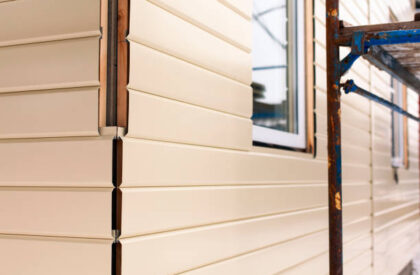 House corner with beige siding covering the walls and scaffolding. Focus on corner. Closeup.