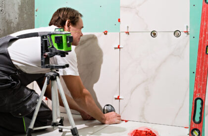 Professional master man laying ceramic tiles on wall in bathroom. Portrait of an experienced repairman laying large size porcelain tiles.Construction worker checking tile installation with laser level